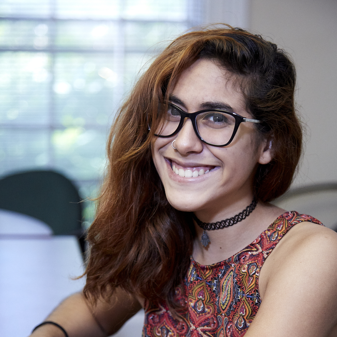 Woman with long brown hair wearing black glasses and a colorful shirt