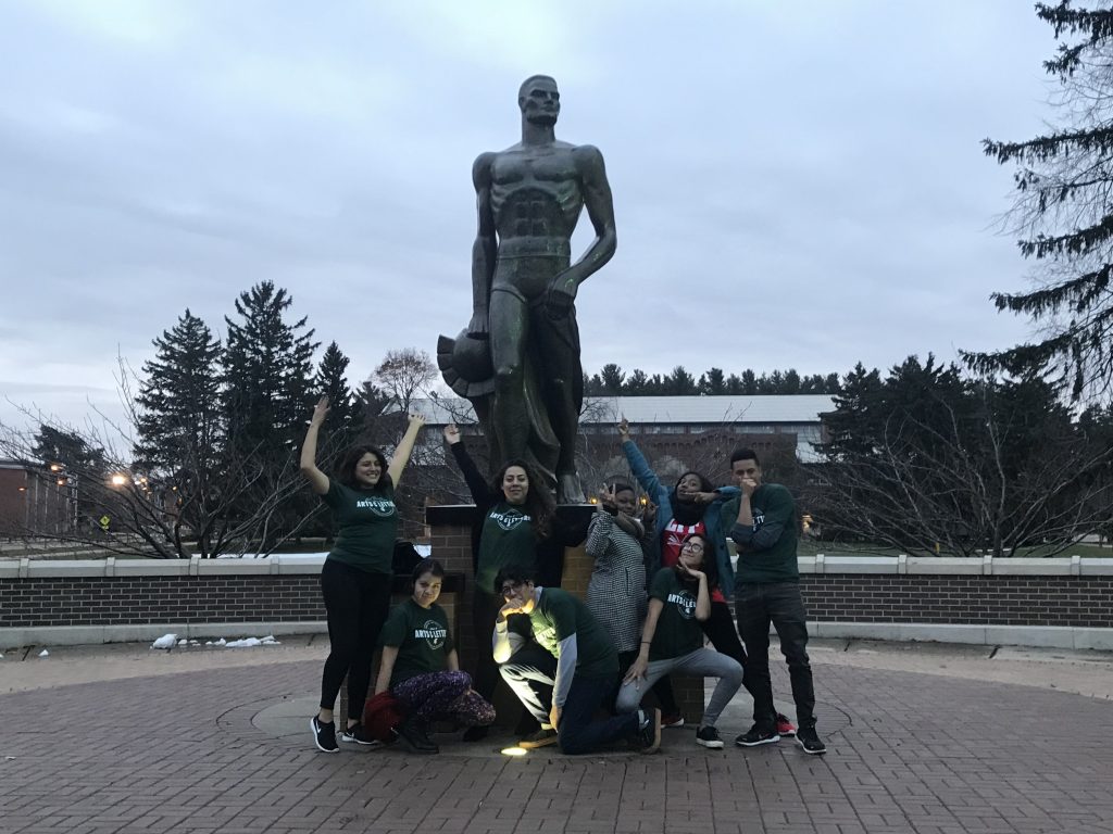 group of students in MSU College of Arts and Letters tshirts posing in front of a statue of Sparty