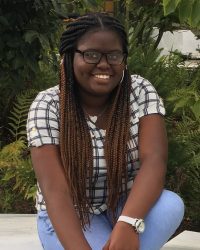 woman in checkered shirt and jeans poses with a big smile outside on a bench